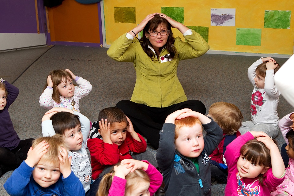 Photo of a teacher and preschool students sitting down on the floor